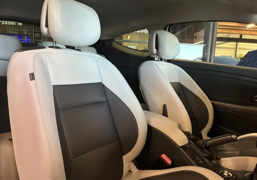 Intérieur de la Renault Mégane Coupé 2.0 DCI 165 GT 2014, vue côté gauche sur sièges cuir bicolores blanc et noir.