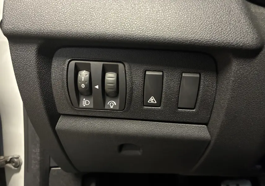 Gros plan sur les commandes de réglage des phares et du tableau de bord dans une Renault Mégane Coupé blanc 2014.