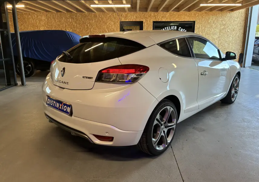 Renault Mégane Coupé blanc vue 3/4 arrière droit en intérieur, avec jantes alliage et feux arrière LED distinctifs.