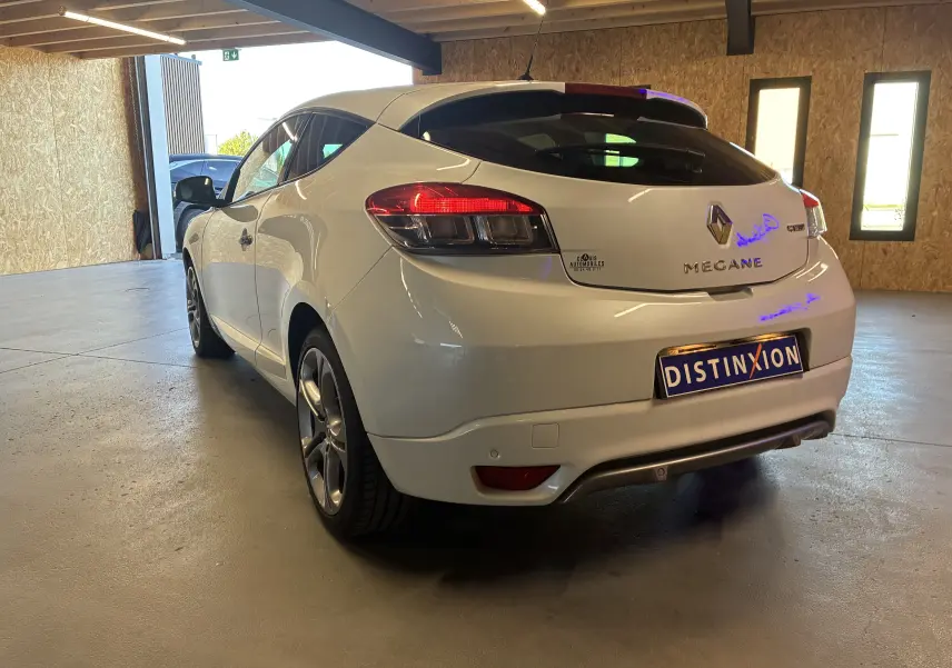 Vue 3/4 arrière droite d'une Renault Mégane Coupé blanche de 2014, avec feux arrière allumés en intérieur.