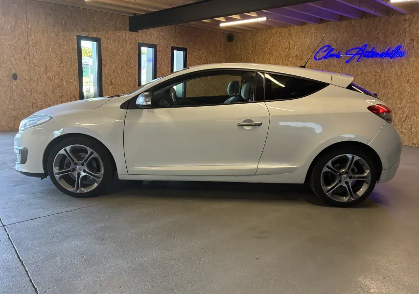 Profil droit d'une Renault Mégane Coupé blanche de 2014, avec jantes alliage et vitres teintées, en intérieur showroom.