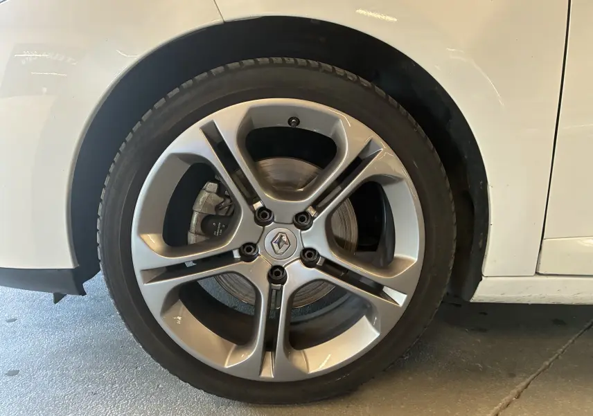 Gros plan sur la roue avant droite d'une Renault Mégane Coupé blanche, mettant en valeur la jante alliage à cinq branches.