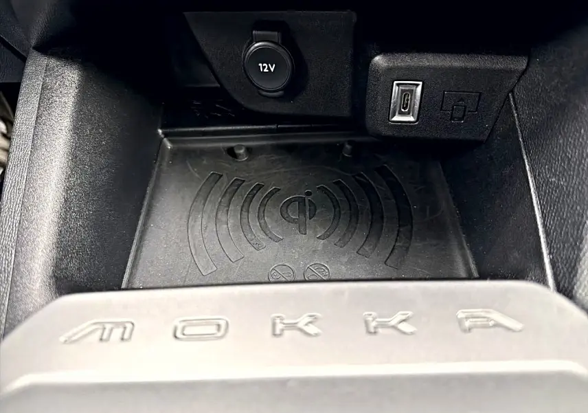 Gros plan sur le compartiment de chargement sans fil et prises USB/12V dans l'habitacle noir de l'Opel Mokka.