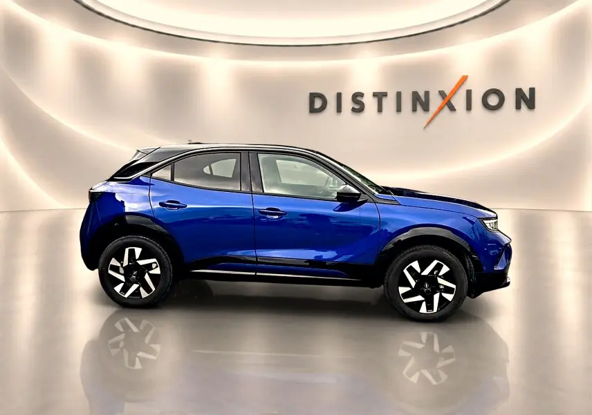 Profil droit de l'Opel Mokka 1.2 turbo bleu 2025 avec jantes noires et toit noir dans un showroom lumineux.