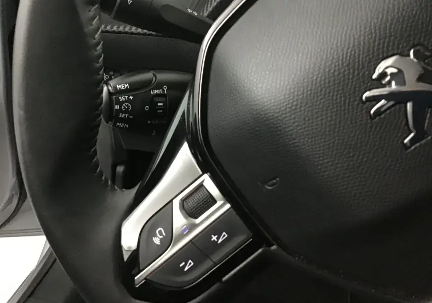 Gros plan sur le volant noir de la Peugeot 208 2022, mettant en valeur les commandes intégrées et le logo lion chromé.