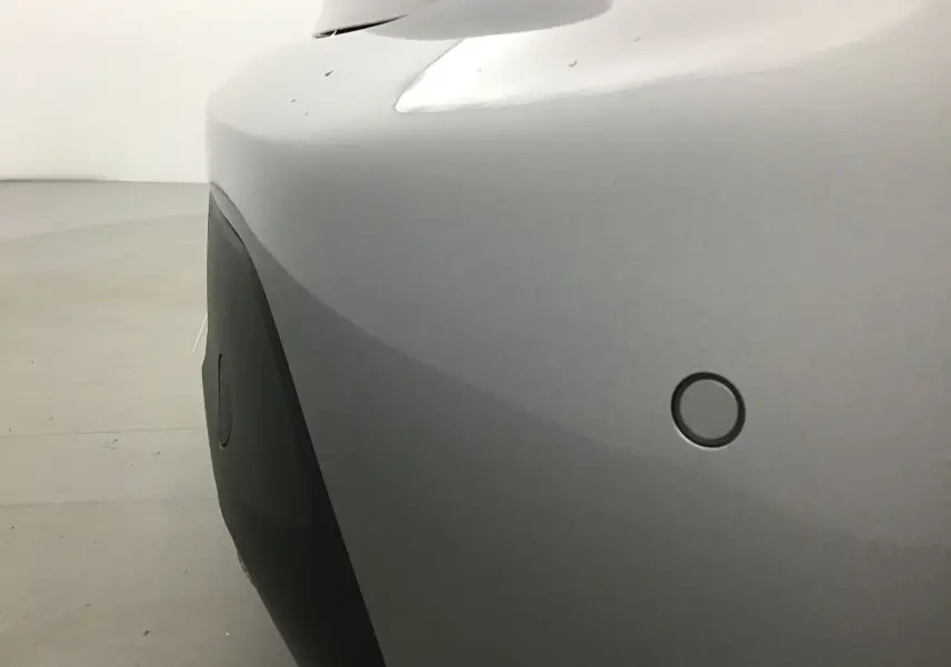 Gros plan sur le pare-chocs avant gris Artense du Peugeot 208 1.2 PureTech 100 Style avec capteur de stationnement.