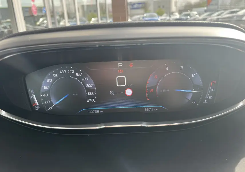 Vue rapprochée du tableau de bord numérique du Peugeot 3008 blanc, affichant compteur vitesse, compte-tours et kilométrage.