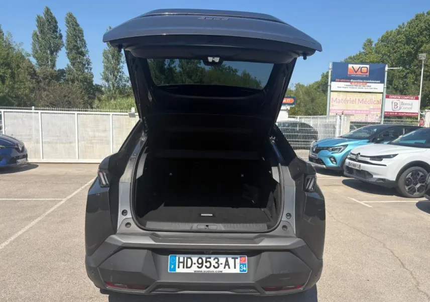 Vue arrière d’un Peugeot 3008 Hybrid gris 2025 avec coffre ouvert sur parking ensoleillé.