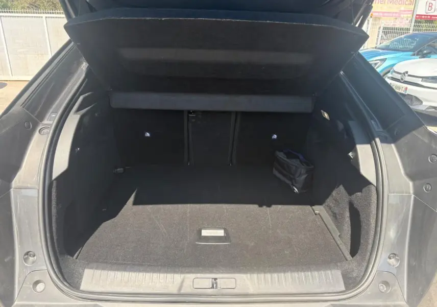 Coffre ouvert vu de l'arrière d'un Peugeot 3008 Hybrid gris, montrant un espace de chargement propre et spacieux.