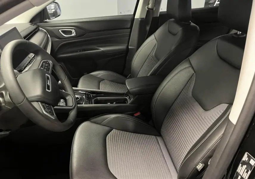 Intérieur avant du Jeep Compass 2024, sièges mixte noir et gris, volant multifonctions et console centrale brillante.