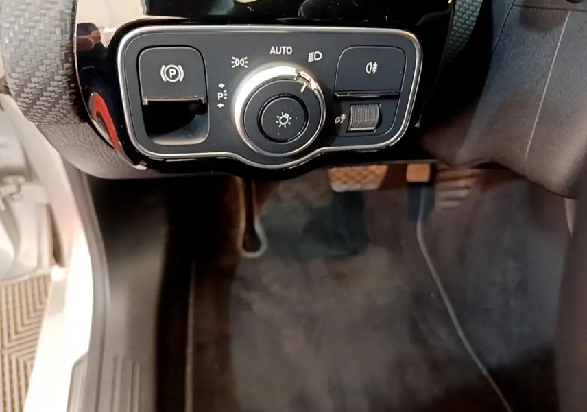 Gros plan sur les commandes d'éclairage et frein à main électrique côté gauche dans l'habitacle d'une Mercedes Classe A gris clair.