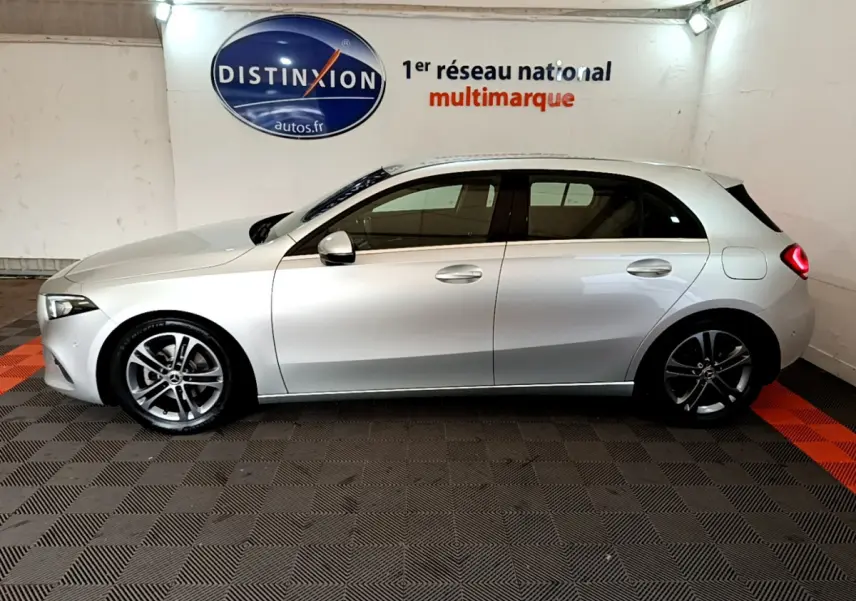 Profil côté gauche d'une Mercedes Classe A gris clair 2020 garée en intérieur sur sol à damier noir et orange.