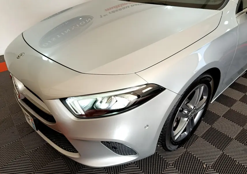 Vue 3/4 avant droit d'une Mercedes Classe A A 180 d Business Line gris clair avec phares LED allumés et jantes alliage.