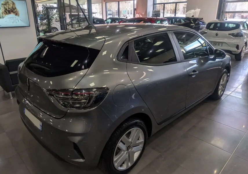 Vue 3/4 arrière droit d'une Renault Clio V Blue dCi 100 CH Evolution gris schiste en showroom, avec feux arrière LED distinctifs.