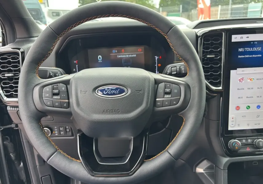 Vue rapprochée du volant cuir noir avec surpiqûres marron du Ford Ranger 2025, tableau de bord digital et écran tactile visible.