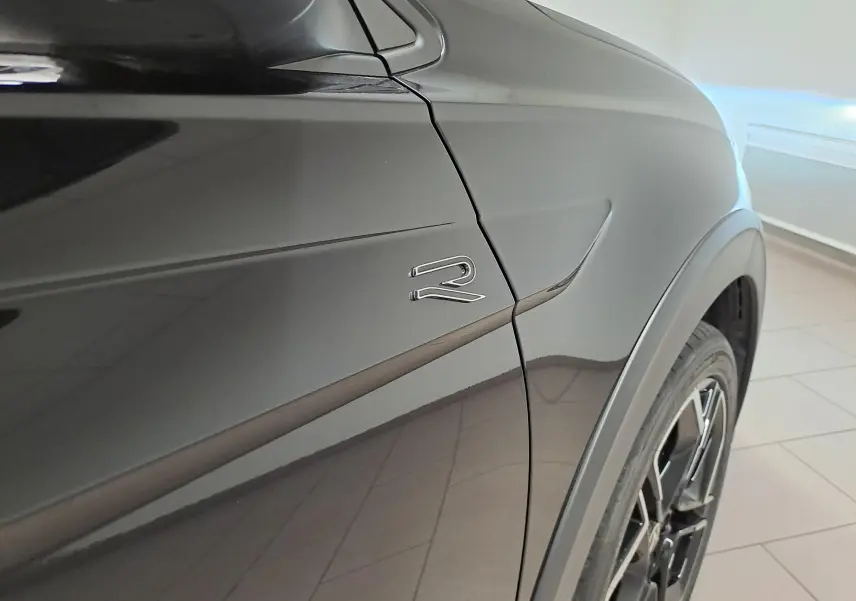Détail du logo R sur la porte côté gauche d’un Volkswagen Taigo noir intense nacré, avec jante et passage de roue visibles.
