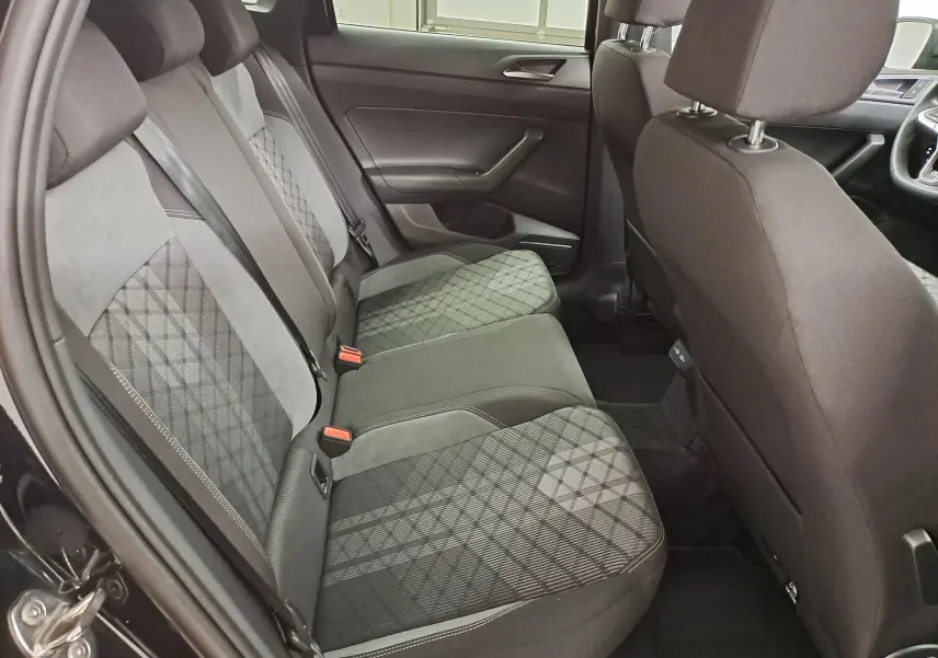 Vue intérieure côté arrière gauche du Volkswagen Taigo 2025, sièges tissu noir à motifs géométriques et garnitures sombres.