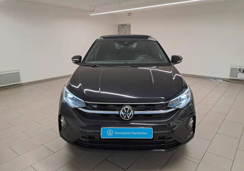 Vue avant d'un Volkswagen Taigo noir intense nacré avec calandre R-Line et toit ouvrant électrique en verre dans un showroom.