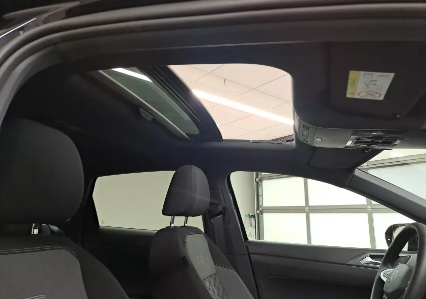 Vue intérieure côté conducteur du Volkswagen Taigo 2025 avec toit ouvrant électrique et sièges sport noirs.