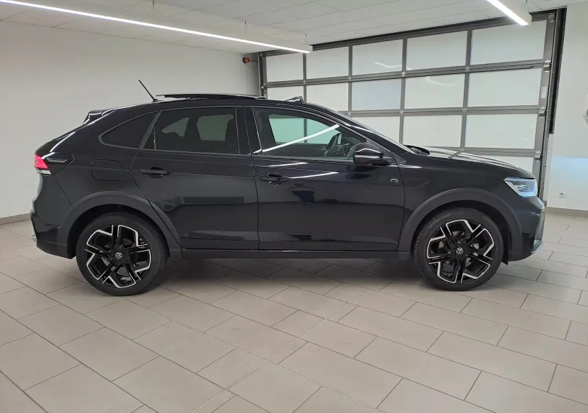 Vue de profil côté gauche d'un Volkswagen Taigo noir intense nacré avec jantes alliage R-Line dans un showroom.