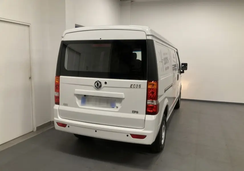 Vue 3/4 arrière d'un utilitaire blanc DFSK EC35 Ecocity électrique, avec feux arrière et logo visibles dans un garage.