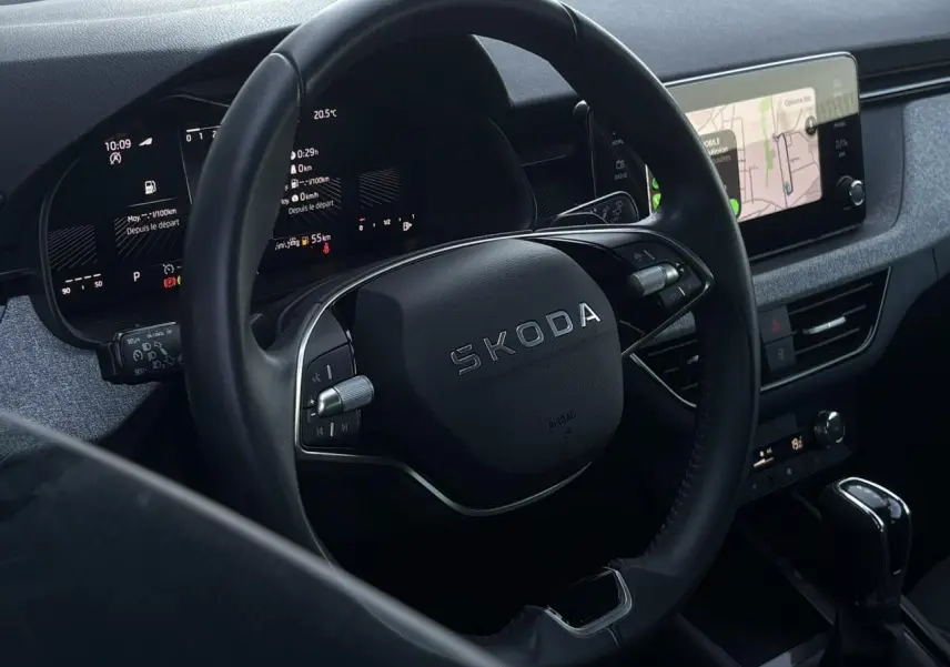 Vue rapprochée du volant noir Skoda avec tableau de bord digital et écran tactile de navigation à droite.