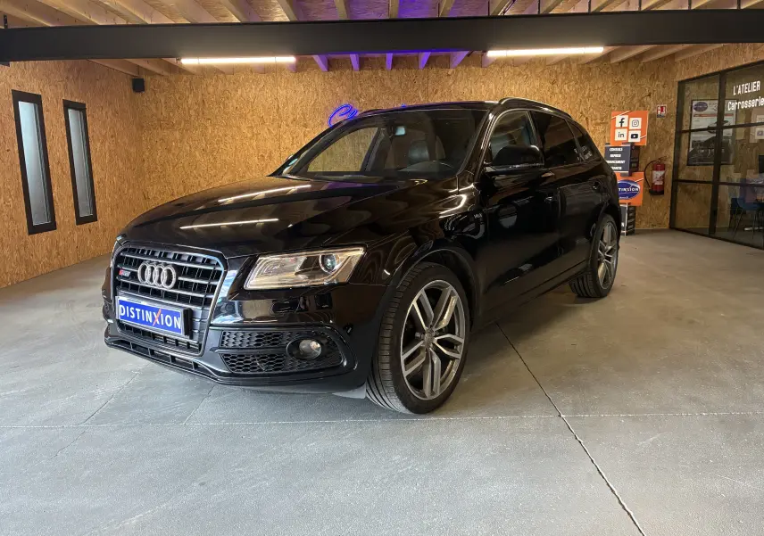Audi SQ5 noir vue 3/4 avant droit, avec jantes alu et calandre distinctive dans un intérieur bois clair.