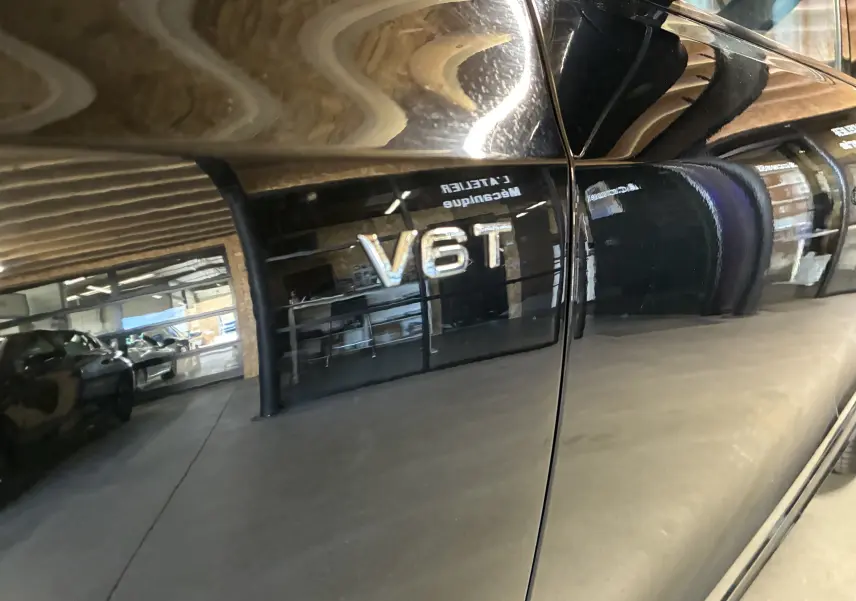 Gros plan sur l’inscription V6T sur la porte noire brillante d’un Audi SQ5, reflet d’un garage en arrière-plan.