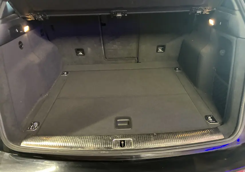 Coffre ouvert vu de l'arrière d'un Audi SQ5 noir, avec tapis de sol et éclairage intérieur latéral allumé.