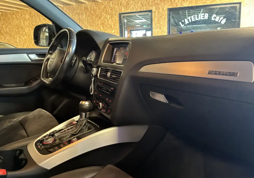 Vue intérieure côté conducteur de l'Audi SQ5 noire, avec tableau de bord, volant cuir multifonctions et console centrale.