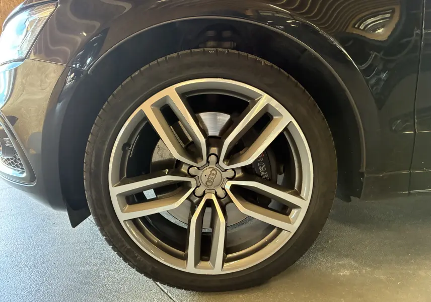 Gros plan sur la roue avant gauche d’un Audi SQ5 noir, avec jante alu à cinq branches doubles et logo Audi central.