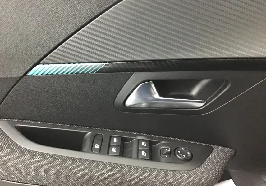 Poignée intérieure côté gauche de la Peugeot 208 gris Artense avec commandes de vitres et décor carbone bleu.