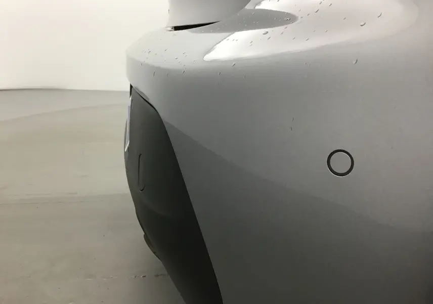 Gros plan sur le pare-chocs arrière gris Artense d'une Peugeot 208 2022 avec capteur de stationnement circulaire visible.