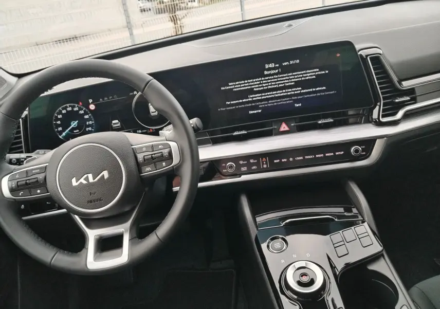 Vue intérieure du tableau de bord et volant KIA Sportage 2025, avec écran tactile large et commandes au volant.