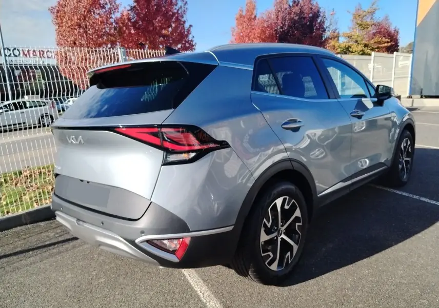 KIA SPORTAGE gris perle en 3/4 arrière droit, avec jantes bicolores et feux arrière LED distinctifs.