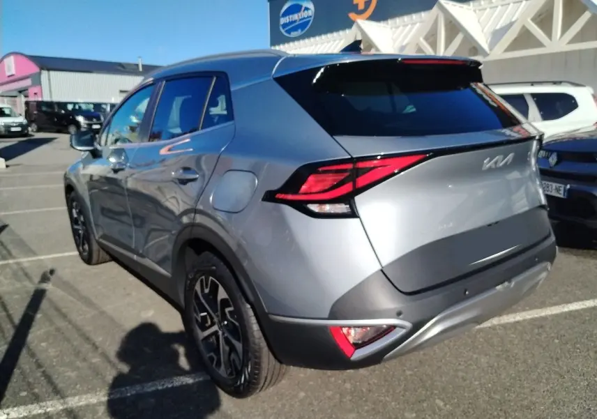 Vue 3/4 arrière droite du KIA Sportage gris perle 2025 avec feux arrière LED et jantes noires bicolores.
