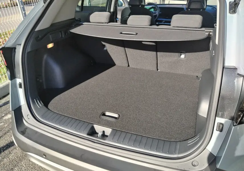 Coffre ouvert vu de l'arrière d'un KIA Sportage gris perle 2025, avec cache-bagages et intérieur noir.