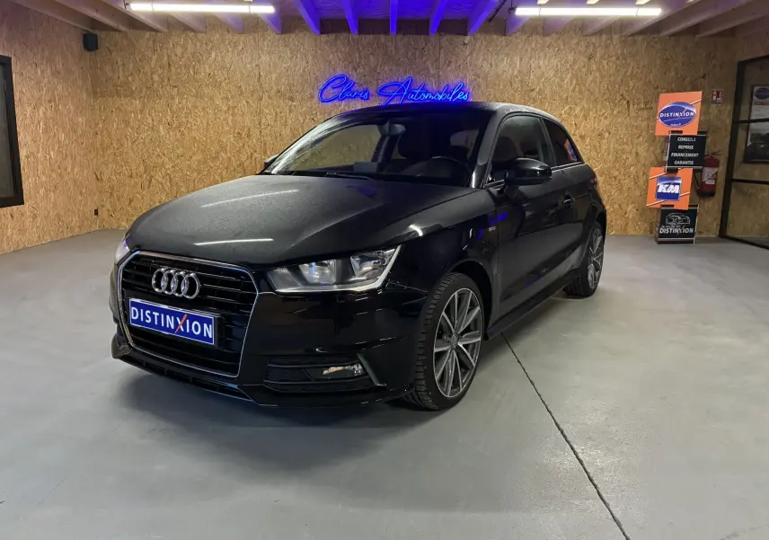 Audi A1 noir en 3/4 avant droit, avec jantes alliage et calandre S-Line visible dans un showroom intérieur.