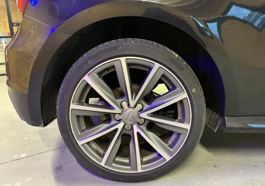 Gros plan sur la roue avant droite d’une Audi A1 noire de 2016, avec jante alliage S-Line à dix branches.