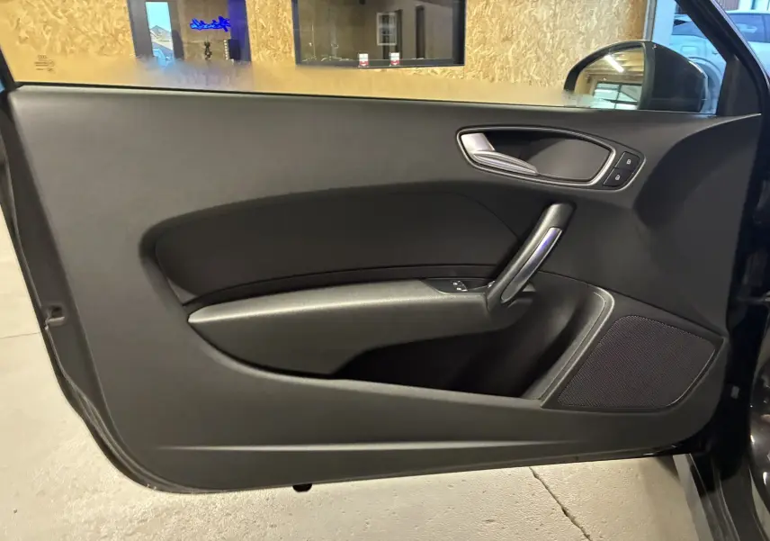 Vue intérieure de la porte côté conducteur noire de l'Audi A1 1.0 TFSI S-Line avec poignée argentée et haut-parleur intégré.