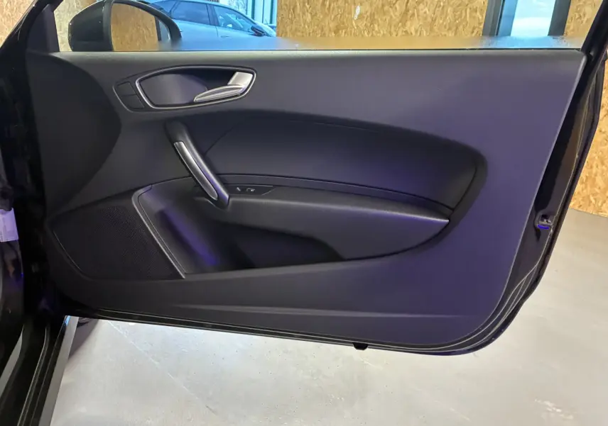 Vue intérieure de la porte côté gauche noire de l'Audi A1 1.0 TFSI S-Line avec poignée argentée et haut-parleur intégré.