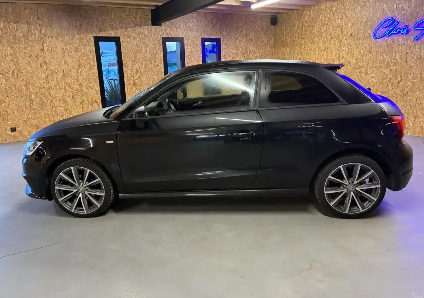 Profil côté gauche d'une Audi A1 noire 3 portes, version S-Line avec jantes alliage 17 pouces dans un intérieur bois.