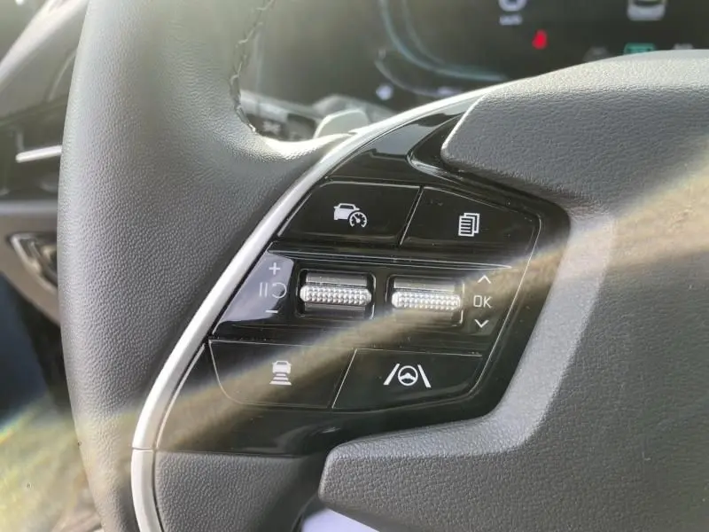 Gros plan sur les commandes du volant côté gauche du KIA Niro 2024 bleu métal, avec boutons d’aide à la conduite.