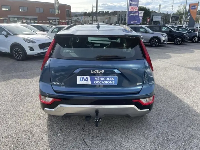 Vue arrière d’un KIA NIRO bleu métal 2024 avec attelage et badge hybride visible sur un parking extérieur.