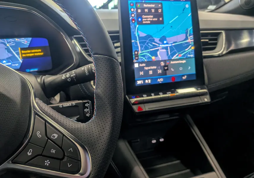 Vue intérieure centrée sur le volant et l’écran tactile du tableau de bord du Renault Symbioz gris Cassiopé, version hybride.