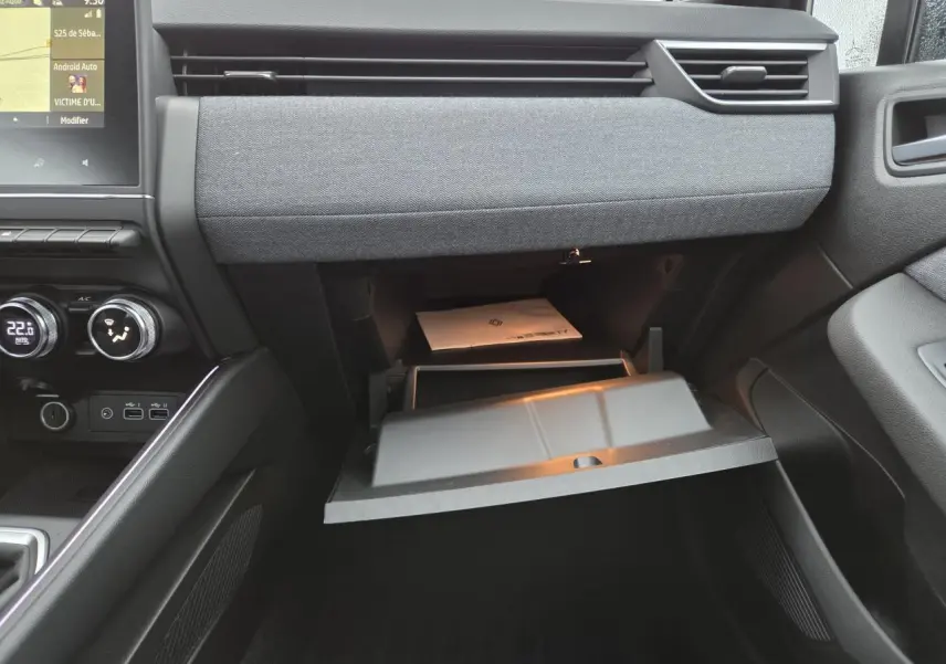 Intérieur avant droit de la Renault Clio 2025 gris schiste, tableau de bord avec boîte à gants ouverte et écran tactile visible.