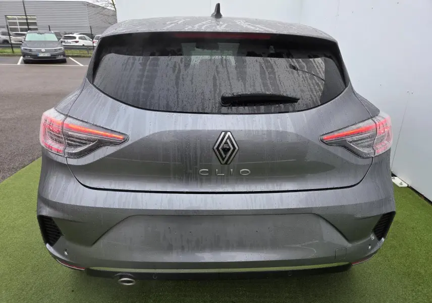Vue arrière d'une Renault Clio gris schiste métal 2025 avec feux LED et vitre arrière surteintée sous la pluie.