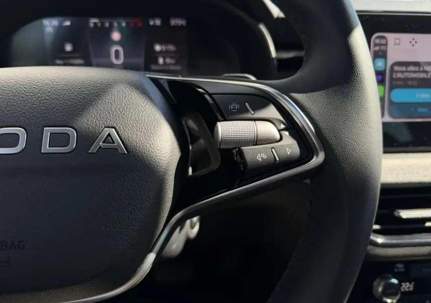 Gros plan sur le volant cuir noir du Skoda Scala 2025, avec commandes multifonctions et tableau de bord numérique flou en arrière-plan.