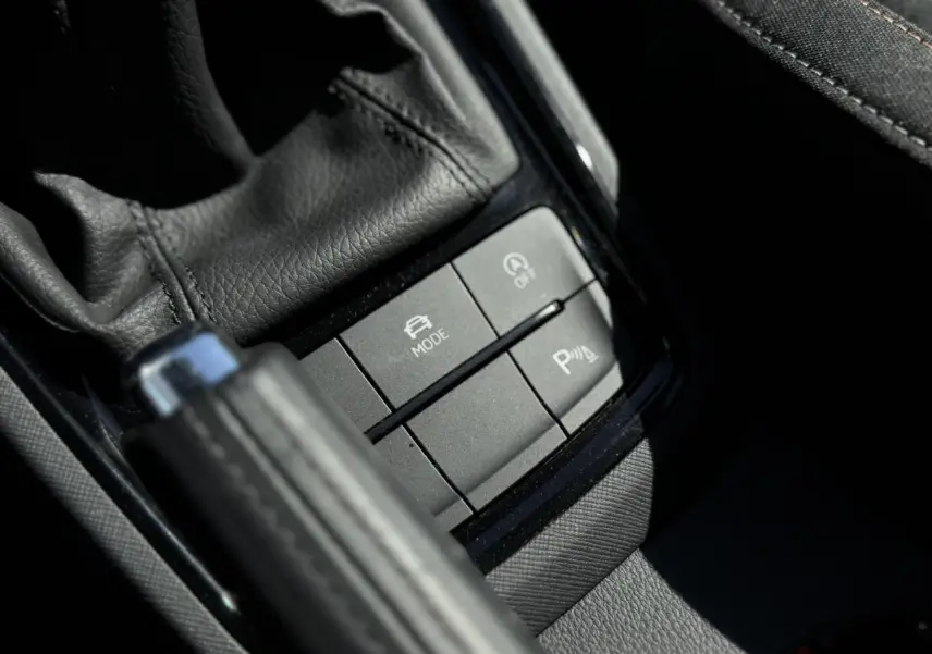 Gros plan sur les commandes noires près du levier de frein à main en cuir dans l'habitacle d'une Skoda Scala 2025.