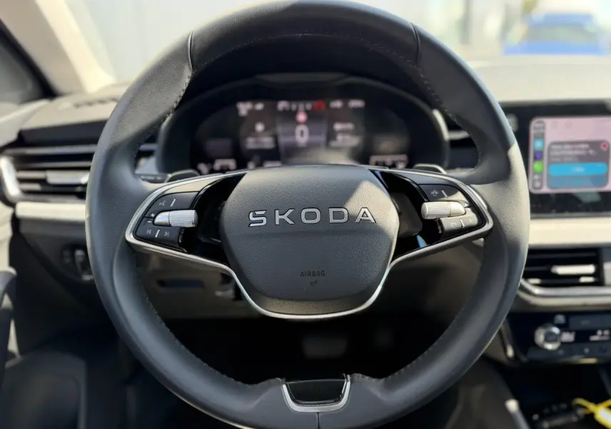 Gros plan sur le volant cuir multifonctions SKODA d'une SCALA 2025, avec tableau de bord numérique en arrière-plan flou.